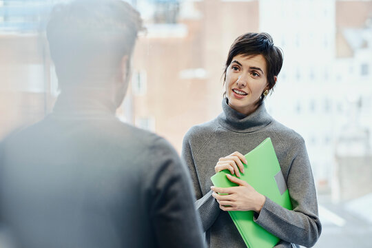 Young businesswoman holding file folder talking with colleague in office