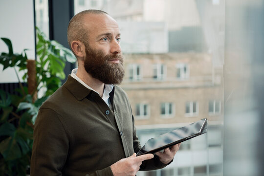 Bearded businessman with tablet PC near glass wall at office