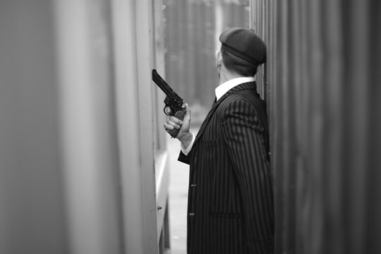 Dangerous retro mobster holding gun while hiding in narrow alley with copy space