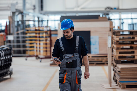 Craftsman in a factory wearing a hard hat and using a smartphone
