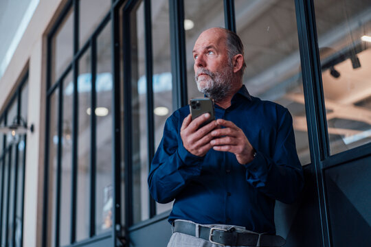 Experienced engineer taking a break in a modern office holding a smartphone