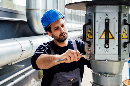 Craftsman in blue helmet performing maintenance on industrial equipment outdoors
