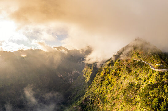 Golden sunlight pierces mist over mountain road in Madeira