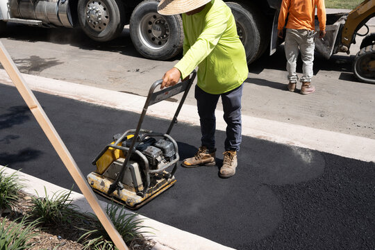 man working with Plate Compactor and Dump Truck on Fresh Asphalt Roadwork