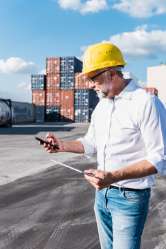 Logistics manager using mobile phone and tablet at cargo terminal