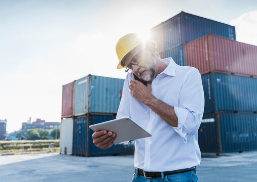 Logistics manager with tablet and mobile at container port