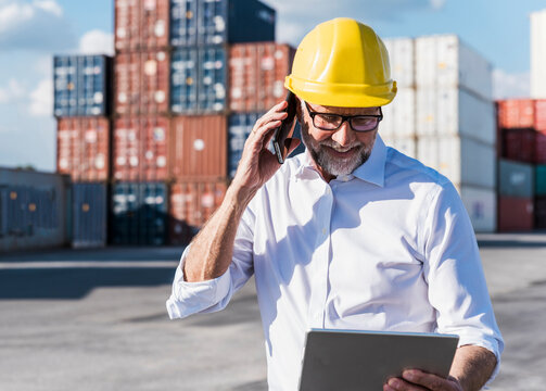 Smiling manager calling and holding tablet outdoors at container port