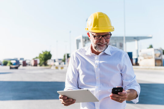 Smiling engineer holding tablet and smartphone at logistics site