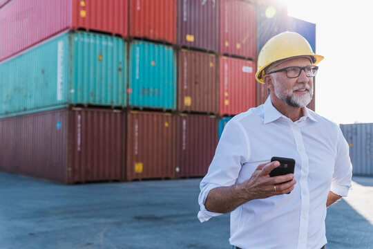Manager holding smartphone outside near shipping container