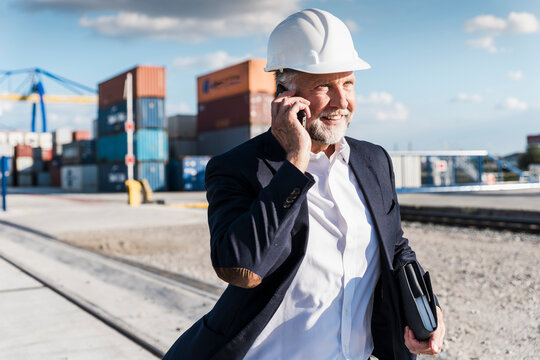 Smiling manager talking on mobile phone outdoors at shipping port
