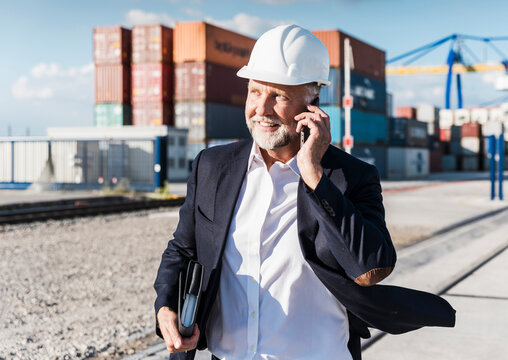Smiling manager in helmet talking on mobile phone at outdoor port