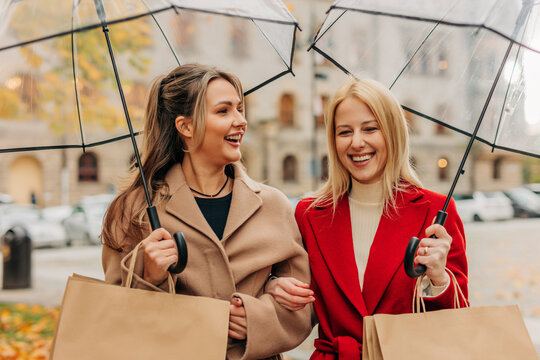 Women laughing and shopping under umbrellas in city on autumn day