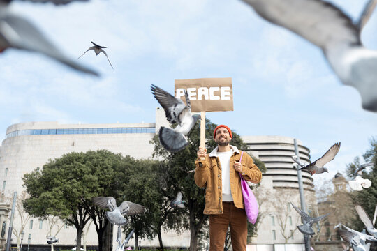 Smiling activist holding peace sign with flying bird outdoors