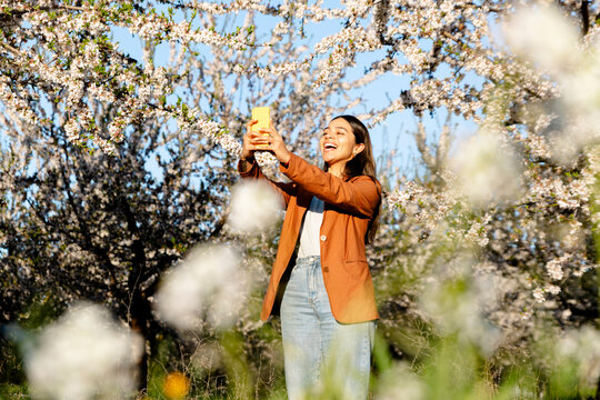 Happy woman taking selfie among blooming spring trees