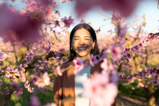 Smiling woman among blooming peach trees in spring