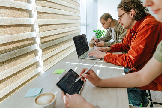 Programmers coding on laptop and digital tablet in sunny office