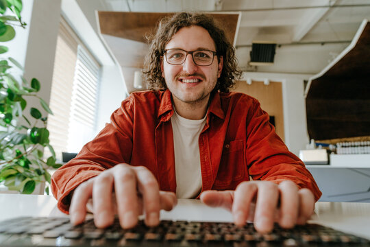 Smiling programmer typing on keyboard working in modern office