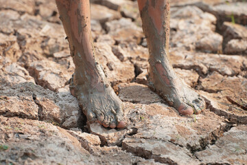 Fototapeta premium Parched Earth: A close-up of a person's feet, caked in mud and standing on cracked, dry earth, illustrating the harsh realities of drought and environmental hardship.