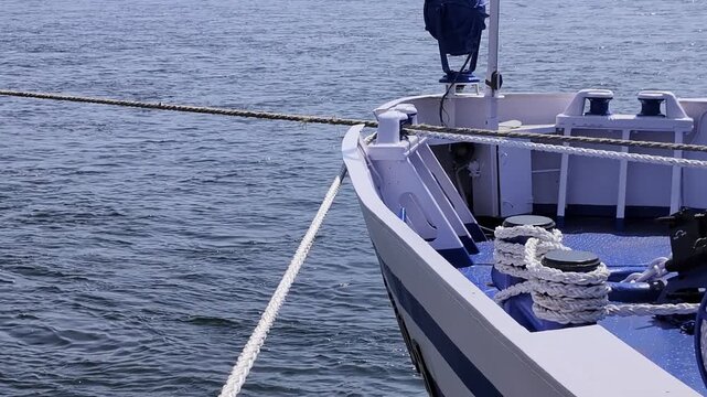 Close-up view of boat bow tied with thick ropes floating on calm water surface. Detailed look at nautical equipment including mooring lines and bollards on vessel deck under daylight.