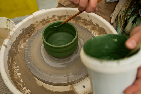 Close up of a paintbrush tip applying green underglaze to a rotating pottery bowl.