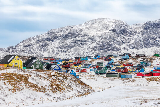 Colorful Greenlandic Inuit houses spread across a snowy hillside below a large mountain in a winter village landscape, Narsaq, Kujalleq, Greenland