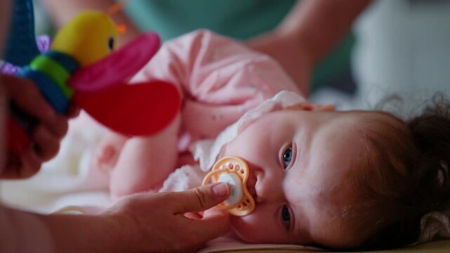 Baby lying sideways on a treatment table while adults provide gentle support and use a colorful toy for stimulation