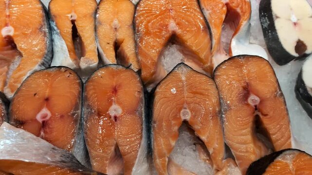 Close-up image of fresh salmon steaks and white fish steaks displayed on a bed of crushed ice. The salmon pieces reveal rich orange flesh with distinct texture while the white fish sections exhibit a.