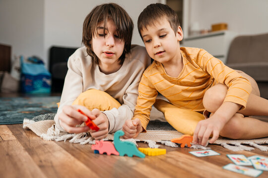 Siblings playing with dinosaur toys on the floor at home