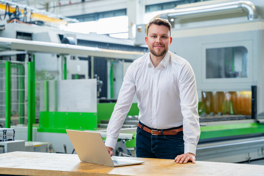 A satisfied manager stands with a laptop in a production hall