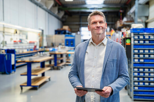 Smiling manager holding digital tablet in factory production hall