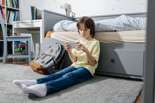 Student sitting on floor distracted by smartphone before school