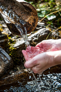Hand catching fresh spring water from a wooden trough outdoors