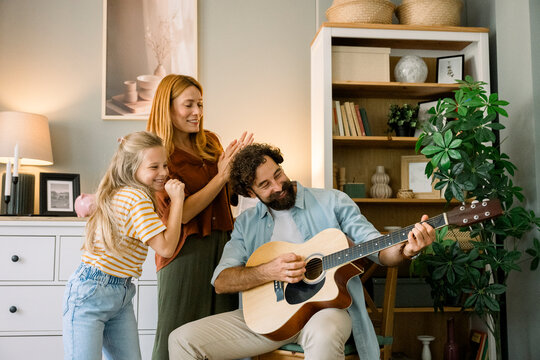Father playing guitar while mother and child dance and laugh at home
