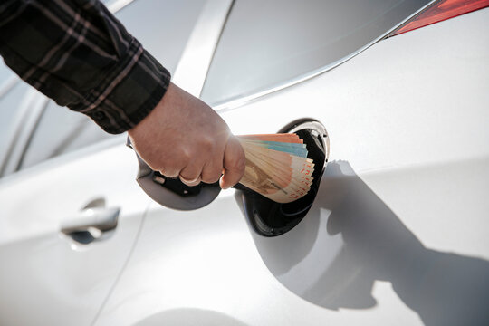 Hand putting cash into a car tank showing high fuel cost