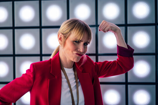 Playful blond businesswoman puckering and flexing muscles in front of illuminated wall at office