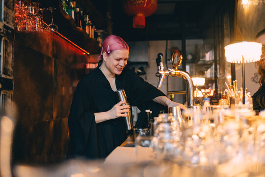 Smiling bartender with pink hair mixing a cocktail at the bar