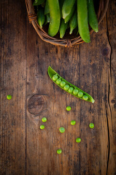 Fresh pea pod and wicker basket on rustic dark wooden table