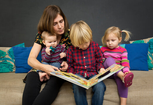 Mother reading book to children on sofa indoors in the Netherlands