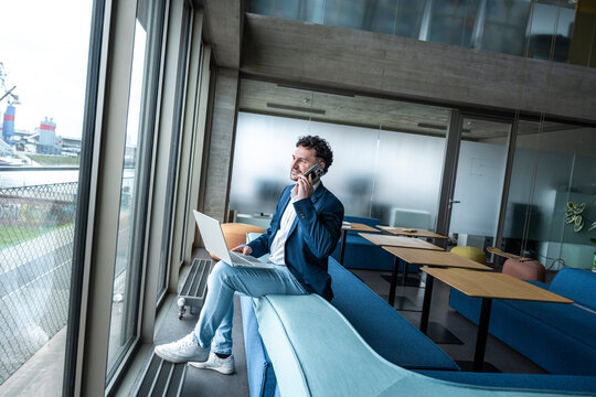 Businessman working on laptop and talking on mobile in modern office