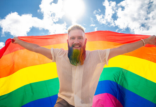 young happy homosexual man with rainbow flag on sky background