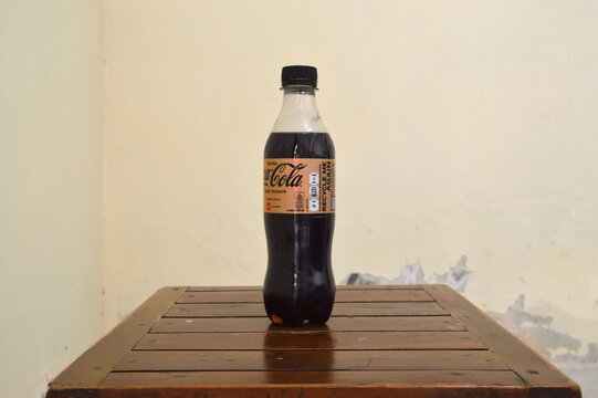 A side profile view of a plastic bottle of Coca Cola zero sugar vanilla flavor highlighting the recycling message and nutritional facts panel on a wooden table.
