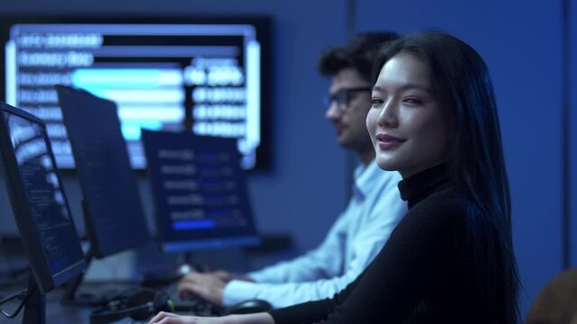 Portrait of smiling female software engineer writing program code on multiple desktop screens in a modern office.
