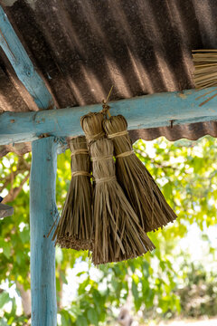 Three bundles of straw from a traditional broom hang under a colorful blue roof in an old house in the Dominican Republic.