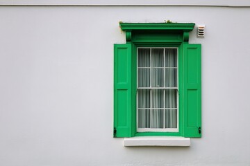 Obraz premium Green wooden window with white curtains and decorative trim set against a plain white wall, showcasing architectural details and vibrant color contrast