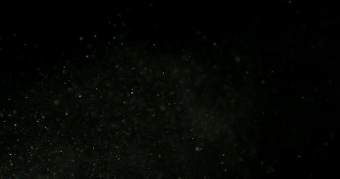 Super slow motion fine dust particles floating through the air on a black background. Subtle atmospheric SFX overlay with soft drifting specks, cinematic texture and dark visual effect.
