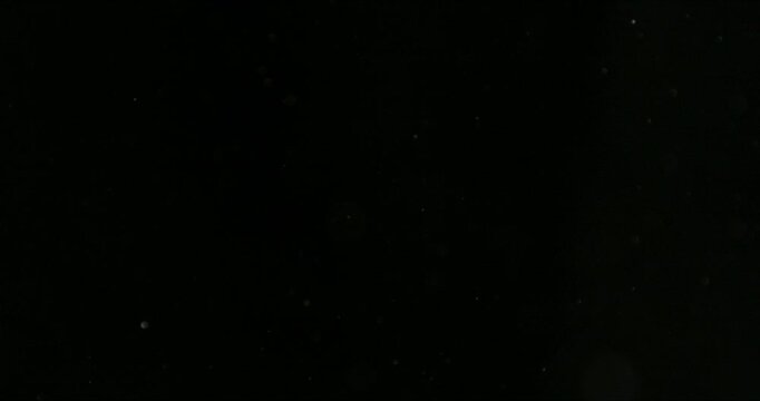 Super slow motion fine dust particles floating through the air on a black background. Subtle atmospheric SFX overlay with soft drifting specks, cinematic texture and dark visual effect.
