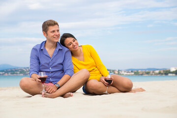 Fototapeta premium Couple sitting on beach with wine glasses, relaxing together