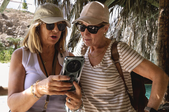 Two Mature Women Friends Checking Smartphone Together During Summer Travel