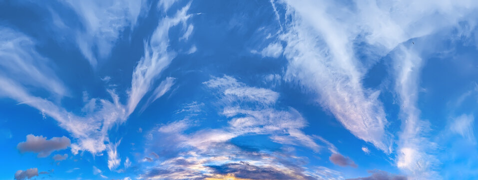 Colorful evening sky at sunset. Flattened flakes of cloud against blue sky. The sun's farewell is exploding to two fun to horizon. A serene landscape of peace and elemental energies.