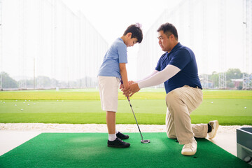 Obraz premium Young boy practicing golf swing with professinoal golf instructor at driving range